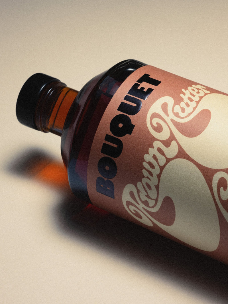 Bottle of Bouquet Brown Butter Caramel infusion on its side. with a rich brown label, bold black BOUQUET logo, and large cream colored graphic. Text reads ‘Brown Butter Caramel’ in groovy cream color script.